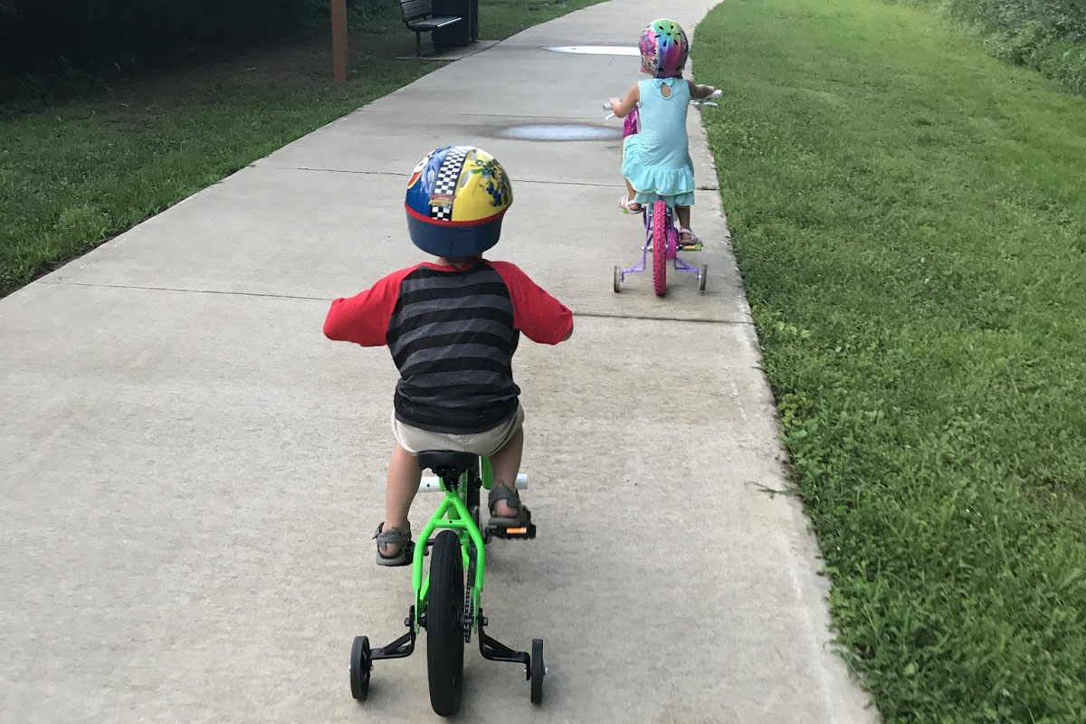 Hai con tập lai xe đạp 3 bánh trẻ em trên đường